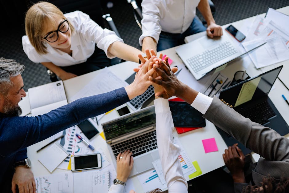 A group of diverse professionals high-fiving over a collaborative workspace