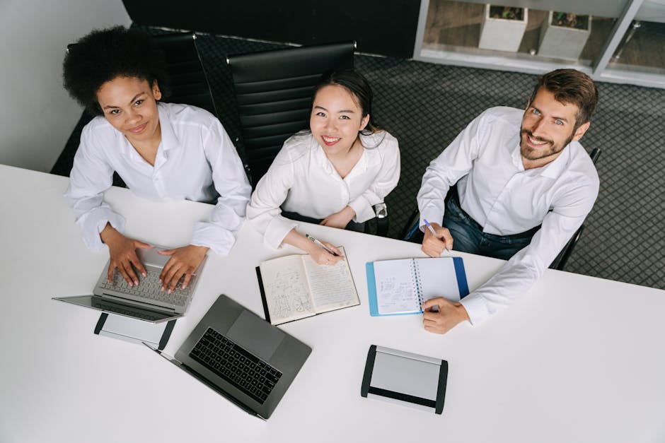 A diverse group of professionals collaborating during an office meeting, using laptops and notebooks